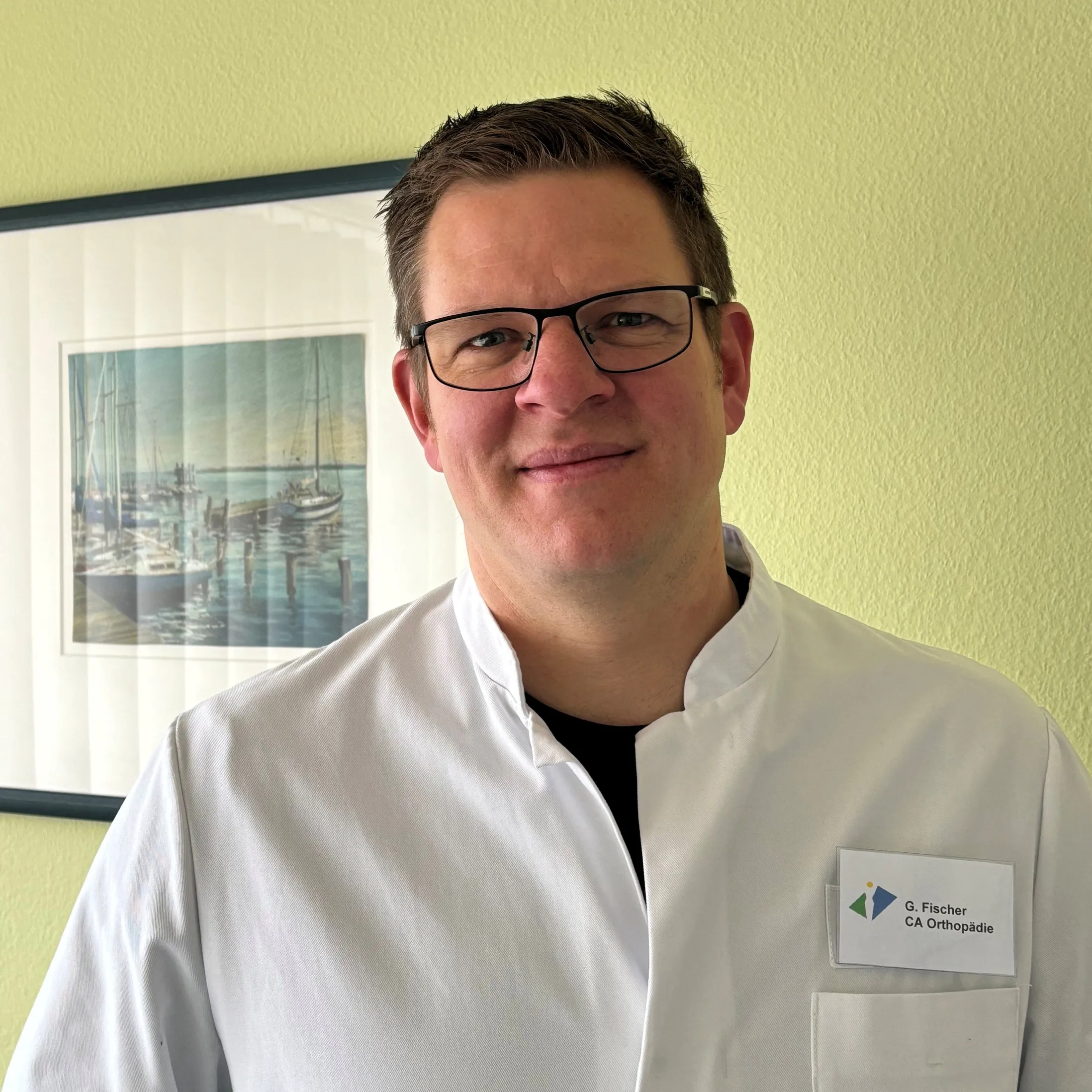 Chefarzt in weißem Kittel vor einem maritimen Kunstwerk an der Wand.