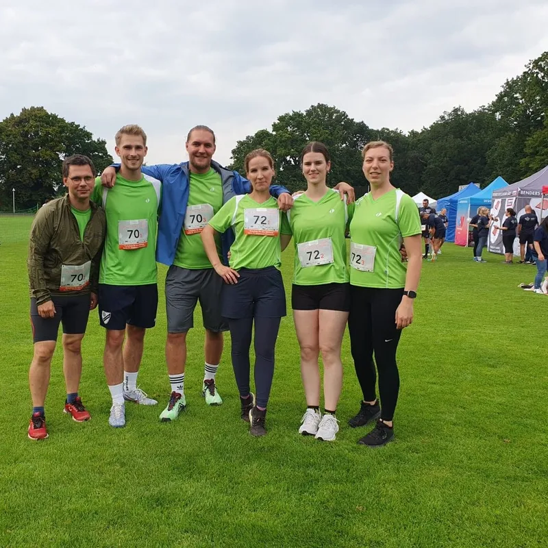 Sechs Teilnehmer in grünen Shirts posieren lächelnd vor einem Firmenlauf-Event.