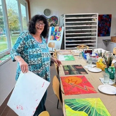 Frau in einem Kunststudio präsentiert ihre farbenfrohen Malereien auf einem Tisch.