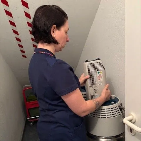 Frau füllt eine Sauerstoffflasche mit einem Gerät in einem engen Raum auf.