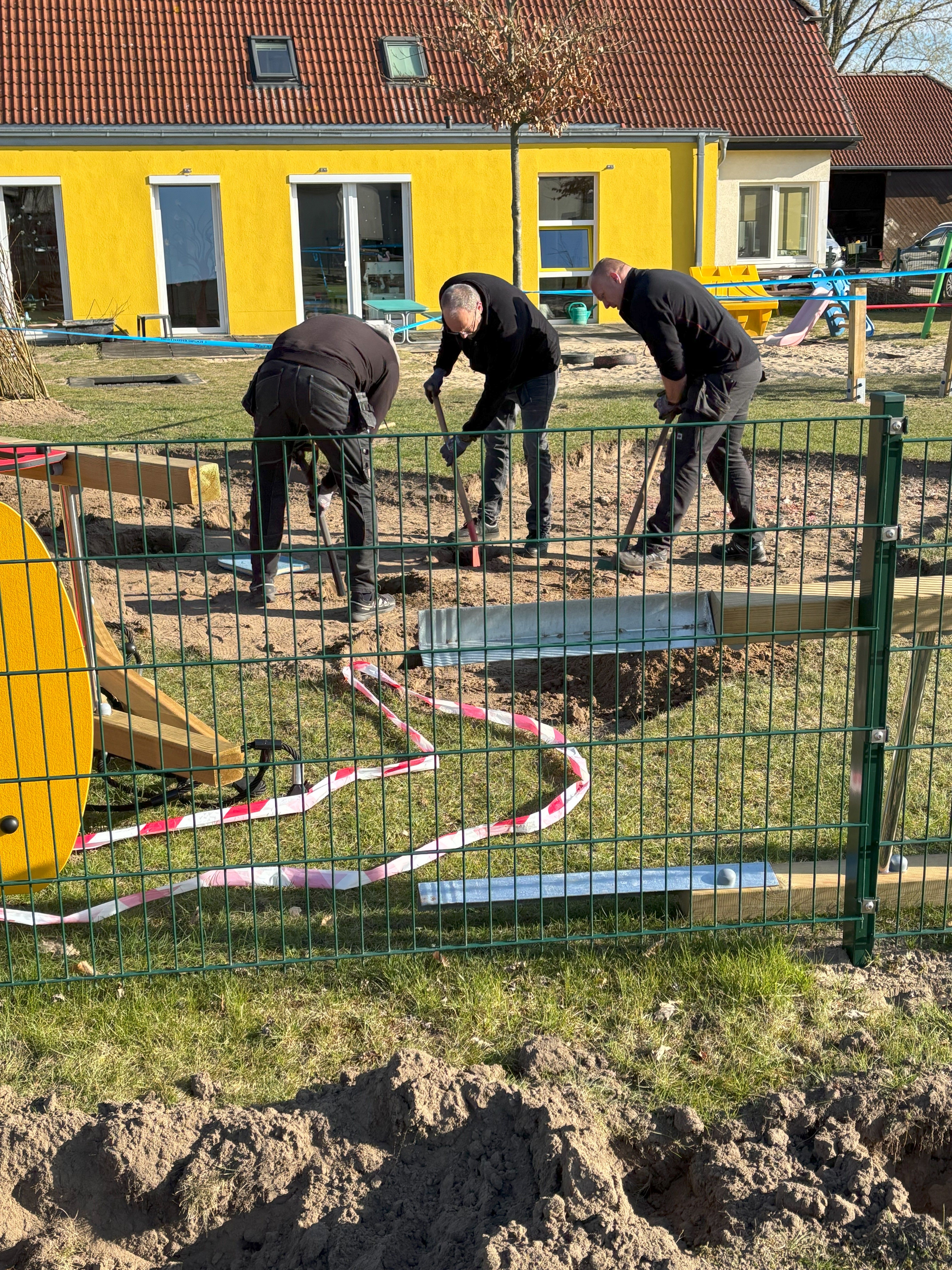 Drei Männer graben auf einem Spielplatz, um neue Spielgeräte zu installieren.
