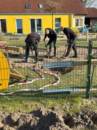 Drei Männer graben auf einem Spielplatz, um neue Spielgeräte zu installieren.