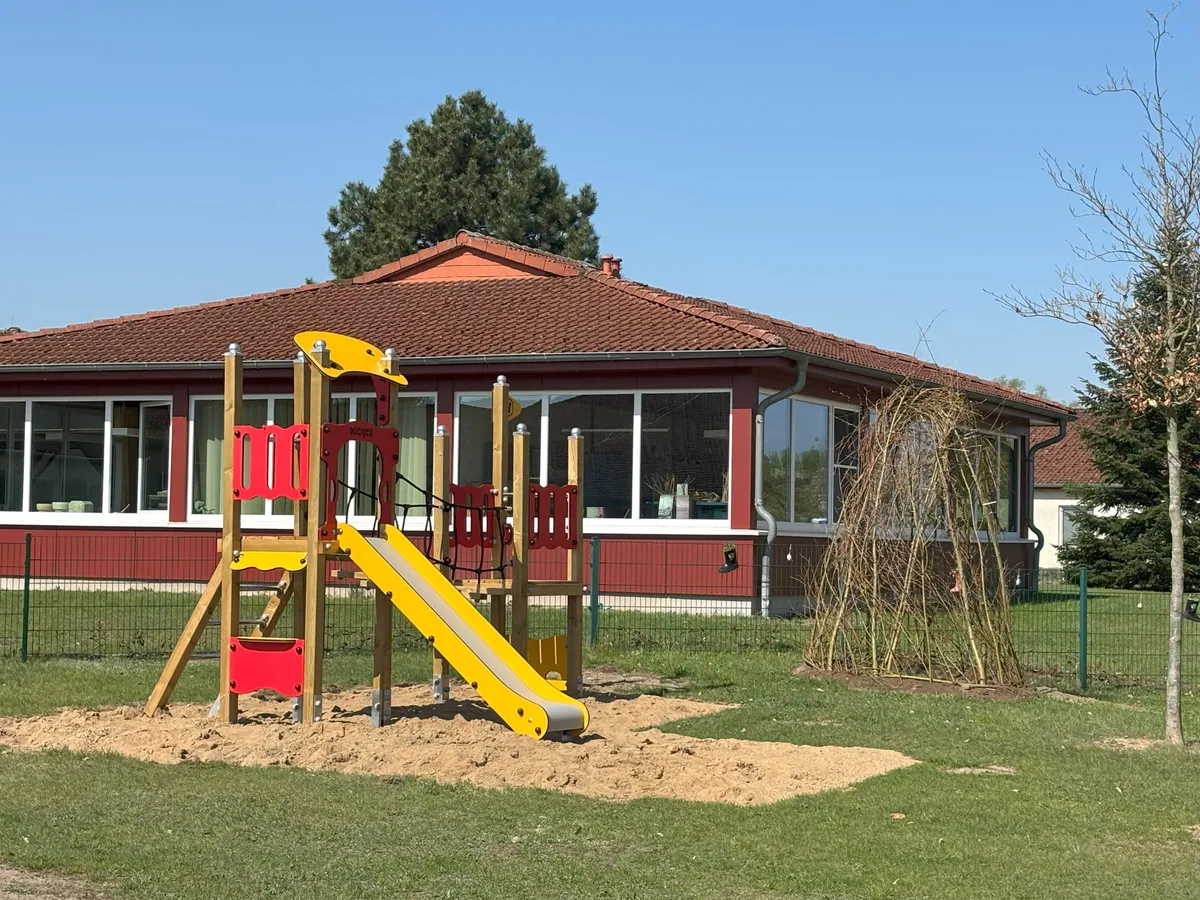 Spielplatz mit Rutsche und Klettergerüst, im Hintergrund ein rotes Gebäude.