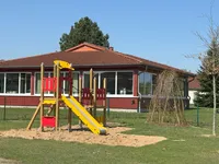 Spielplatz mit Rutsche und Klettergerüst, im Hintergrund ein rotes Gebäude.