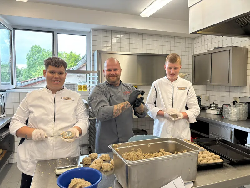 Drei Personen in einer Küche formen Teigbälle, während sie kochen und lernen.