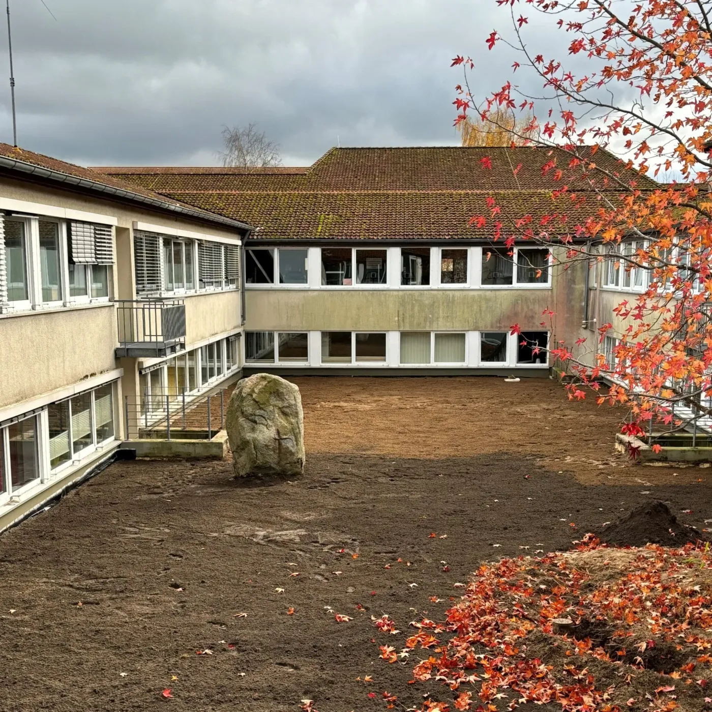 Hinterhof eines Gebäudes mit einem großen Stein und buntem Herbstlaub.