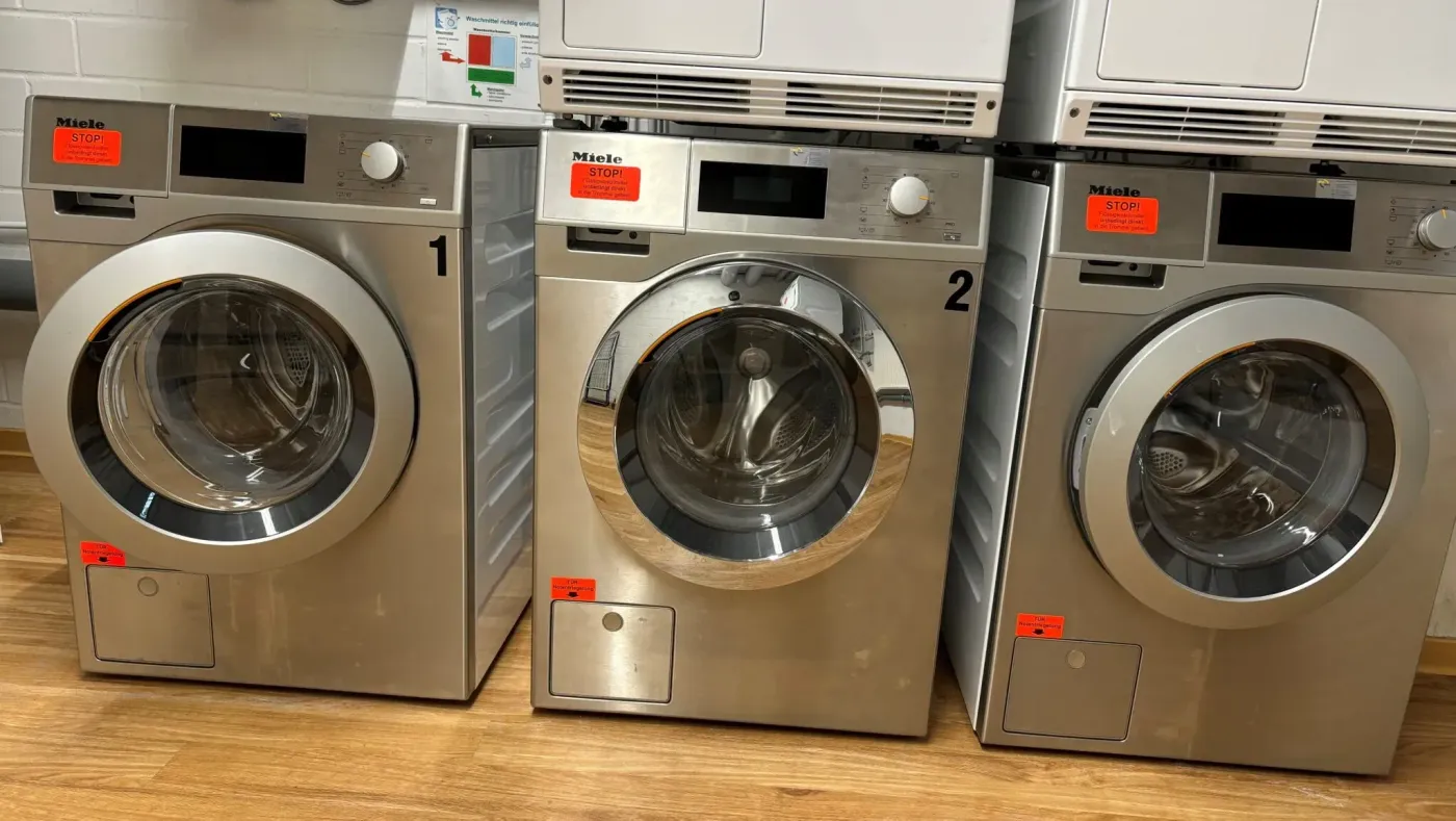 Drei moderne Waschmaschinen der Marke Miele in einem Verkaufsraum auf Holzfußboden.